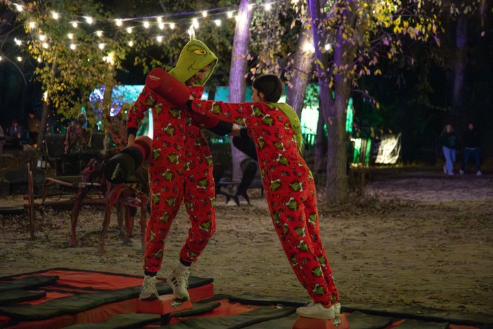 Two people in red onesies have fun on a balance game under string lights outdoors at night.