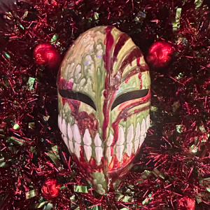 Grinning mask with blood-like streaks on red tinsel backdrop.