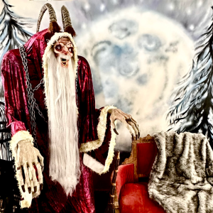 A creepy figure with horns, red robe, and fur trim stands beside a red chair with fur blanket.