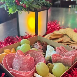 Charcuterie box with meats, cheese, grapes on a table with crackers and holiday decor.