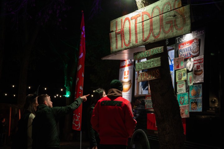 People ordering at a nighttime food truck with a 'HOTDOGS' sign.