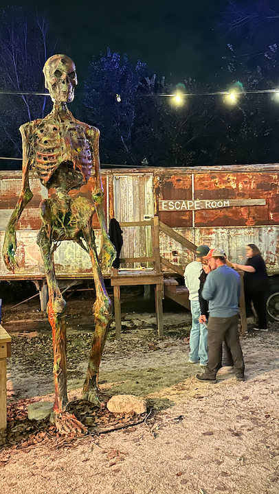Guests at the signed Escape Room entrance beside a towering skeleton