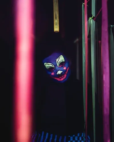 A neon-painted clown peering between hanging tubes on Exiled’s Trail